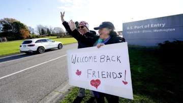 Dual U.S.-Canadian citizen Traysi Spring, right, and her American husband Tom Bakken, hold a homemade sign to welcome people heading into the U.S. from Canada.