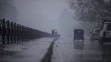 Kashmiris walk as it rains on a cold and foggy day in Srinagar.