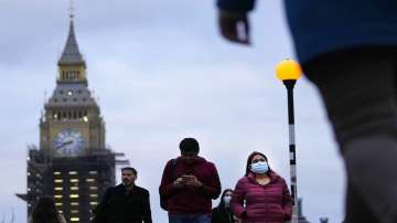 People partly wearing a face-covering walk across Westminster Bridge in London.