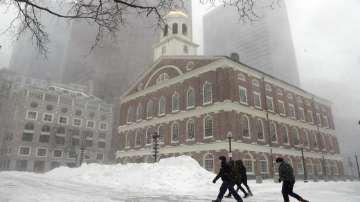 People walk in the snow outside Faneuil Hall, Saturday, Jan. 29, 2022, in Boston. Forecasters watched closely for new snowfall records, especially in Boston, where the heaviest snow was expected late Saturday. 