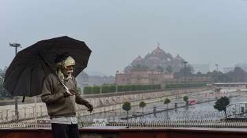 A man uses an umberella during rains, near Akshardham temple, in New Delhi, Saturday, Jan. 8.