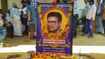 Relatives and friends gather near a garlanded photo of Naveen Shekharappa, to mourn his demise outside his residence at Chalageri village, in Haveri, Wednesday, March 02, 2022. 