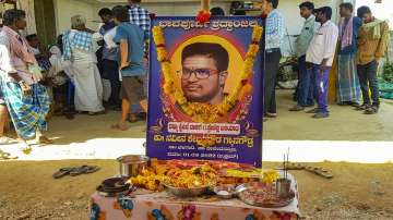 Relatives and friends gather near a garlanded photo of Naveen Shekharappa, to mourn his demise outside his residence at Chalageri village in Haveri