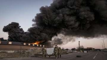 Ukrainian servicemen carry containers backdropped by a blaze at a warehouse after a bombing on the outskirts of Kyiv, Ukraine.