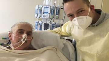 In this photo provided by the University of Maryland School of Medicine, David Bennett Jr., right, stands next to his father's hospital bed in Baltimore, Md., on Jan. 12, 2022, five days after doctors transplanted a pig heart into Bennett Sr., in a last-ditch effort to save his life. Bennett, the first person to receive a heart transplant from a pig died Tuesday, March 8, at the University of Maryland Medical Center, two months after the groundbreaking experiment. His death was announced Wednesday.