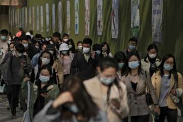 People wearing face masks to help protect from the coronavirus walk by a wall displaying propaganda posters as they head to work at the Central Business District during the morning rush hour