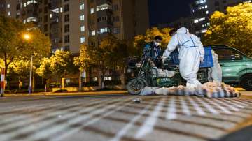 Deliverymen wearing protective suits carry bags of food at the gate of a residential community in Shanghai, China, Monday, April 11, 2022. The U.S. has ordered all non-emergency consular staff to leave Shanghai, which is under a tight lockdown to contain a COVID-19 surge.