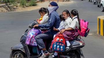 A man shields his face from the heat with a cloth while riding a two-wheeler with children