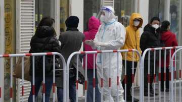 A worker in protective gear speaks to visitors lining up outside a building that was closed off after a case of coronavirus was detected 