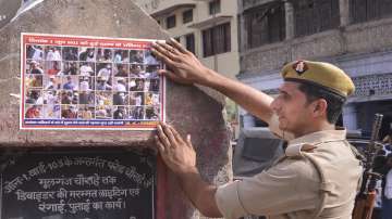 A police person sticks a poster of those accused to be involved in a clash following a controversial remark by suspended BJP leader Nupur Sharma, in Kanpur.