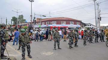 Security personnel stand guard as people from the Kashmiri Pandit community block a road to protest against the killing of the school teacher Rajni Bala, near Srinagar Airport. Bala was shot dead by militants in Kulgam district of South Kashmir.?