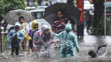School students walk through a flooded street following heavy monsoon rains