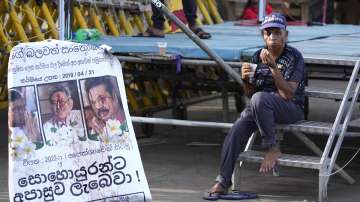 A protester drinks a cup of tea as she sits by a defaced poster carrying portraits of ousted president Gotabaya Rajapaksa, center, and his brothers at the entrance to presidents office in Colombo, Sri Lanka. 