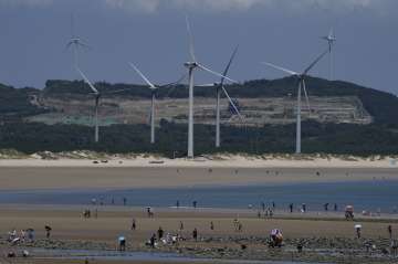 Beachgoers walk near wind turbines along the coast of Pingtan in Southern China's Fujian province 