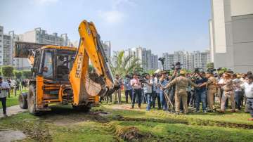 Police personnel guard as a Noida Authority buldozer arrives for the demolition of illegal construction at the Grand Omaxe society, in Noida, Monday, Aug 8, 2022.