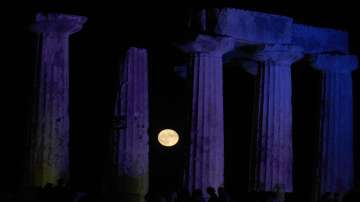 A full moon sets behind the temple of Apollo at the ancient site of Corinth, about 89 kilometers (54 miles) west of Athens, Friday, Aug. 12, 2022.