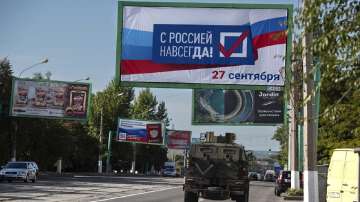 FILE - A military vehicle drives along a street with a billboard that reads: "With Russia forever, September 27", prior to a referendum in Luhansk.