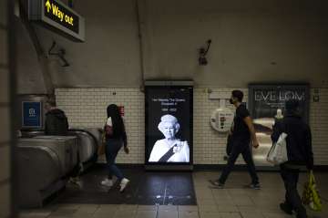 People walk past a photo of Queen Elizabeth II as they walk out of a subway station in London.