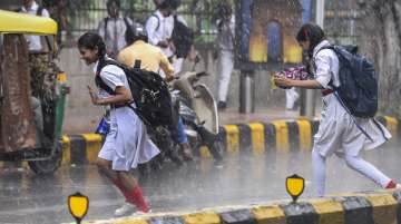New Delhi: Students rush to cross a road amid a monsoon shower, in New Delhi