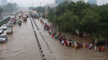 Commuters wade through the waterlogged Delhi-Gurugram Expressway service road after rainfall, in Gurugram. 