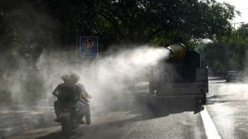 A motorcyclist drives past a Delhi government vehicle sprinkling water to control air pollution in New Delhi.