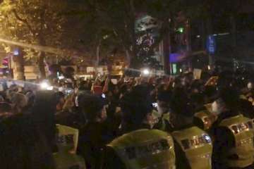 In this image from video obtained by The Associated Press, police, foreground, watch protesters in Shanghai on Saturday, Nov. 26, 2022.