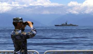 A People's Liberation Army member looks through binoculars during military exercises as a Taiwanese frigate is seen at a distance.