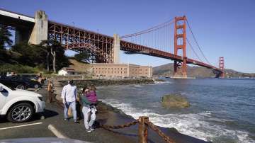 People walk along a seawall with Fort Point and the Golden Gate Bridge in the background in San Francisco.