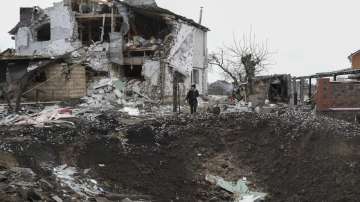 A woman stands on top of a crater next to a destroyed house after a Russian rocket attack in Hlevakha.