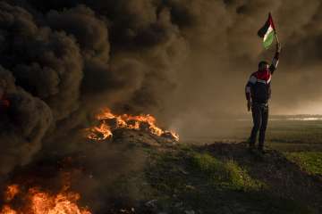 Palestinians burn tires and wave the national flag during a protest against an Israeli military raid in the West Bank city of Jenin, along the border fence with Israel, in east of Gaza City.