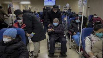 A man pushes an elderly woman past patients receiving intravenous drips in the emergency ward of a hospital.