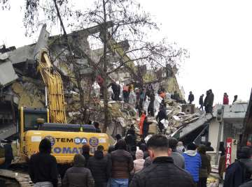 People and emergency teams rescue a person on a stretcher from a collapsed building in Adana.