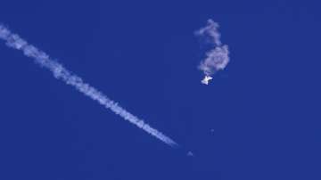 The remnants of a large balloon drift above the Atlantic Ocean, just off the coast of South Carolina, with a fighter jet and its contrail seen below it.