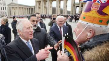 King Charles III of Great Britain, left, greets a fan with a Burger King hat at the Brandenburg Gate