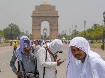 Photographers cover themselves with scarves during a hot summer afternoon, at the India Gate, in New Delhi