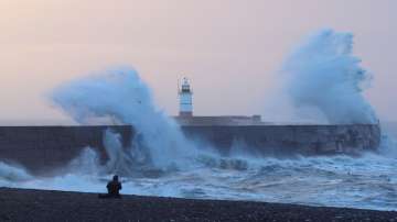 A person views as large waves hit the harbour wall at sunrinse during Storm Isha in Newhaven, southern Britain.