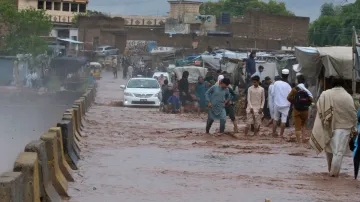 People wade through a flooded bridge on a stream, which is overflowing following heavy rains, on the