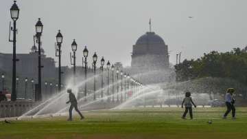 A boy stands facing a spray to beat the heat at Central Vista Lawns near India Gate, in New Delhi.