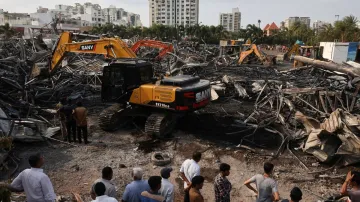 Machines move debris as onlookers watch following a fire in a gaming zone in Rajkot