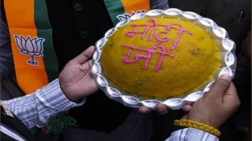 A BJP worker holds a laadoo plate bearing PM Modi's name