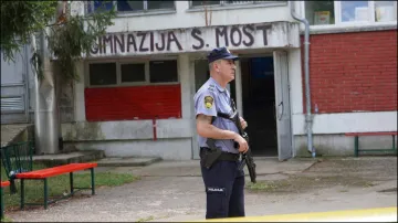 A police officer stands guard outside the building of a high school in Bosnia where a man opened fire killing three staff members.