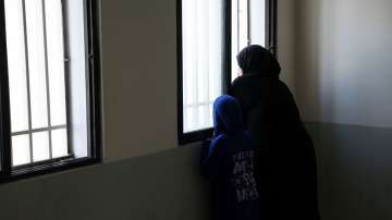 An internally displaced person looks out of a window with a young girl at the Technical Institute of