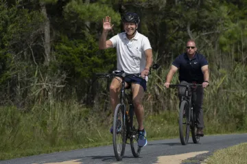 US President Joe Biden waves to a cheering crowd as he rides his bike followed by a Secret Service a