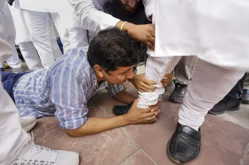 Delhi Minister Saurabh Bharadwaj with other MLAs holds the foot of BJP MLA Vijender Gupta, asking for his support for the reinstatement of bus marshals, in New Delhi.