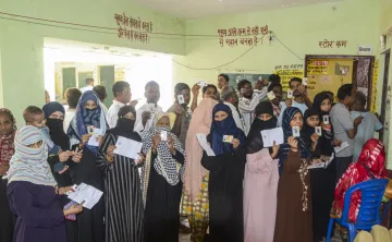 Voters show their identification cards while waiting to cast votes at a polling booth during UPs Sishamau Assembly constituency bypoll