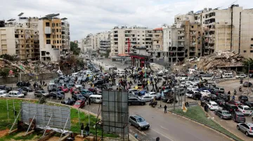 People gather as vehicles drive near damaged buildings, in Beirut's southern suburbs, after a ceasef