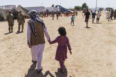 A man walks with a child through Fort Bliss' Do&amp;ntilde;a Ana Village where Afghan refugees are being housed in New Mexico.&amp;nbsp;