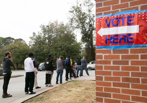 People stand in queue to vote at a polling booth to