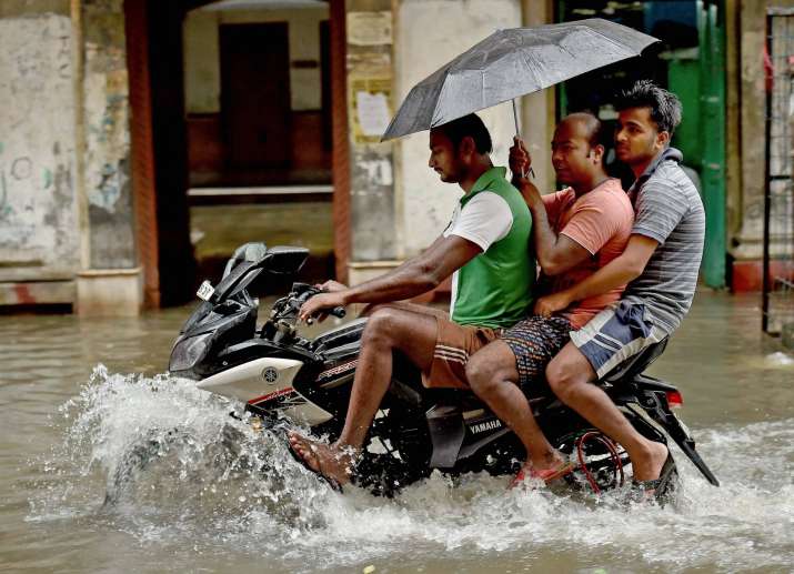 People on a motorcycle wade through a flooded street in