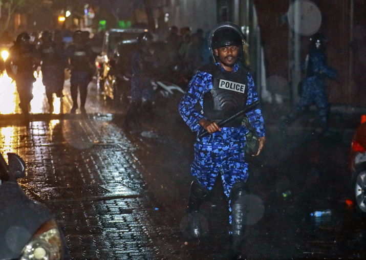 A Maldives policeman charges with baton towards protesters
